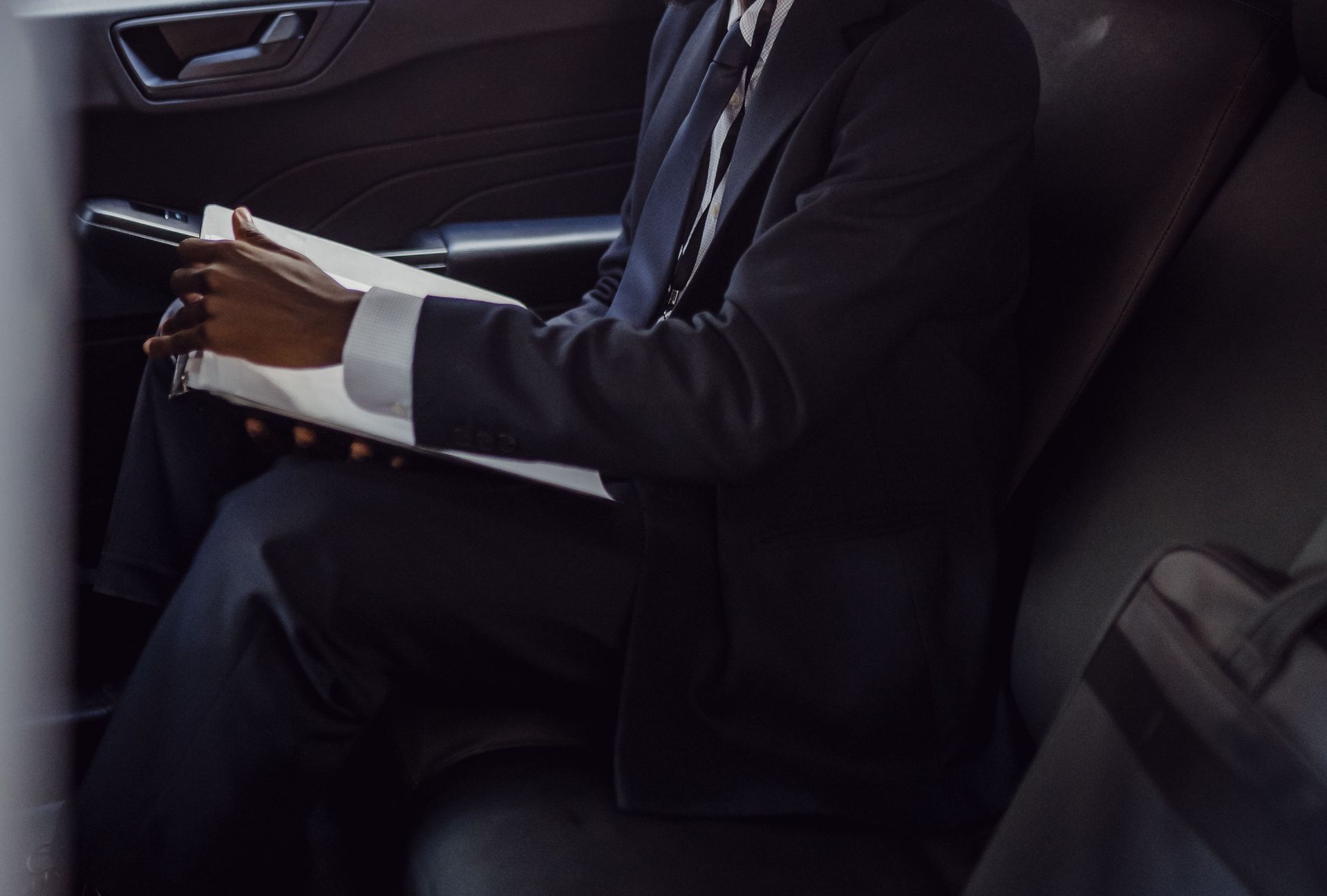 A business professional in a suit reading documents inside a car.